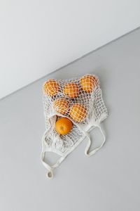 Kaboompics - Six Fresh Oranges in a Cotton Net Bag on a Sunlit Neutral Surface