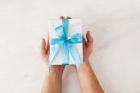 Kaboompics - Top-Down View of Hands Holding a White Christmas Gift with Blue Ribbon