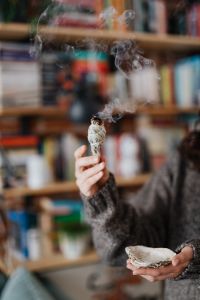 Kaboompics - Sage Smudge Stick with Billowing Smoke in Front of Bookshelves, Home Cleansing