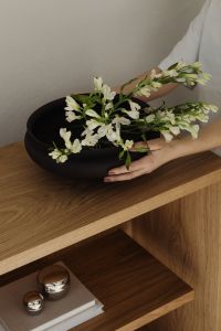 Kaboompics - Woman arranging white flowers in black bowl close-up