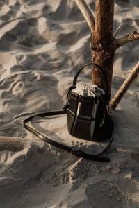 Kaboompics - Black Leather Handbag Resting on Sand beside Driftwood