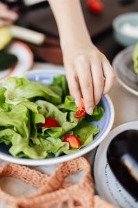 Kaboompics - Hand Garnishing a Blue Bowl of Leafy Green Salad with Cherry Tomatoes
