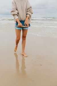 Kaboompics - Woman Carrying a Closed Book with Her Reflection on Wet Sand, Cloudy Baltic Beach