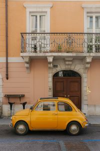 Kaboompics - Yellow Vintage Car Beneath an Ornate Balcony on a Historic Italian Street