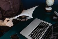 Kaboompics - Person Reading a Magazine Beside a Laptop and Camera