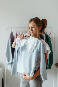 Kaboompics - Smiling Teenage Girl Holding Up a White Eyelet Blouse, Youth Fashion at Home