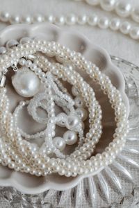 Kaboompics - Layered Pearl Necklaces in Scalloped White Dish on a Faceted Glass Tray, Close-Up