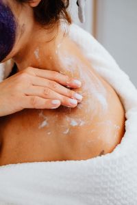 Kaboompics - Woman Applying Skincare Cream to Her Shoulder and Chest in a White Robe