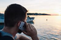 Kaboompics - Man Talking on a Smartphone with a Boat on the Water at Sunset