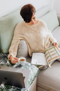 Kaboompics - The woman is drinking tea on the couch, reading the newspaper and using a laptop