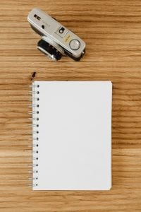 Kaboompics - Compact Silver Camera Above a Blank Spiral Notebook on a Wooden Desk