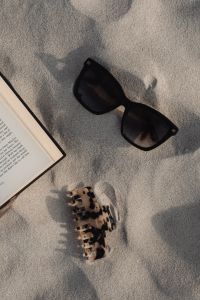 Kaboompics - Black Sunglasses and an Open Book on Textured Beach Sand