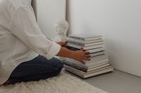 Kaboompics - Woman Arranging Stacked Books Beside a White Bust