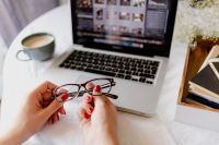 Kaboompics - Close-Up of Hands Holding Eyeglasses over a MacBook beside Coffee on White Bedding