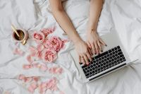 Kaboompics - Woman Working on Laptop beside Pink Roses and Coffee on White Bedding, Work-from-Bed Lifestyle