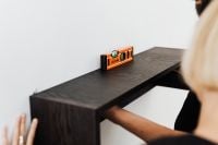 Kaboompics - Hands Fitting a Dark Floating Shelf to a White Wall with a Spirit Level