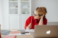Kaboompics - Woman Holding Pencil and Looking Away from Laptop at Creative Work Desk