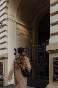 Kaboompics - Woman in Camel Coat Entering a Historic Building Gate