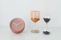 Kaboompics - Rose Quartz Desk Clock and Amber and Black Hourglasses on a Bright Minimalist Surface