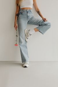Kaboompics - Woman Posing with Raised Leg in Wide-Leg Jeans, White Sneakers and Long-Stem Flower