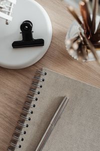 Kaboompics - Black Binder Clip on a White Desk Lamp beside a Spiral Notebook and Silver Pen
