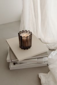 Kaboompics - Ribbed Glass Candle on Stacked Books with Sheer Curtains