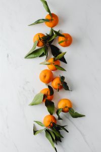 Kaboompics - Vertical Arrangement of Whole Mandarins and Leaves on Marble for Seasonal Food Promotion