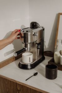 Kaboompics - Hand Pressing Espresso Machine Button Above White Mug