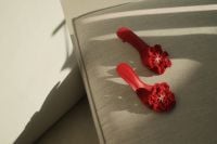 Kaboompics - Red Crochet Flower Sandals on a Sunlit Gray Upholstered Seat, Fashion Still Life