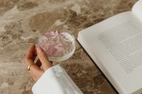 Kaboompics - Hand Holding Glass with Floating Flower Petals beside Open Book
