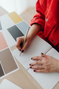 Kaboompics - Red-Sleeved Hand Writing in Notebook beside Oversized Color Swatches, Desk Detail