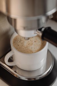 Kaboompics - Foamy Coffee in a White Cup Under Espresso Machine
