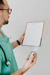 Kaboompics - Doctor Comparing Medicine Bottle and Clipboard
