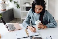 Kaboompics - Asian Woman Writing Notes While Holding a Coffee Cup