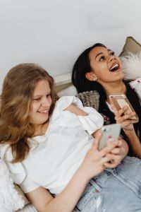 Kaboompics - Laughing Teen Friends Holding Phones During a Cozy Bedroom Hangout
