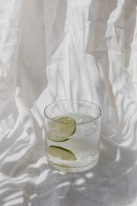 Kaboompics - Tall Lime Water Glass with Ice on Draped White Linen, Soft Minimal Summer Drink Styling