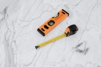 Kaboompics - Vertical Flat Lay of a Spirit Level, Tape Measure and Wall Anchors on Marble