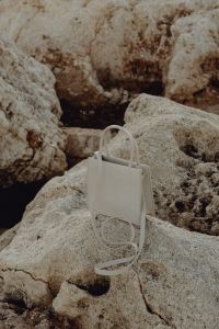 Kaboompics - White Structured Handbag Resting Upright on Coastal Stone