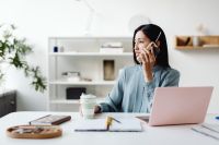 Kaboompics - Asian Woman Taking a Phone Call at a Desk with Laptop and Coffee