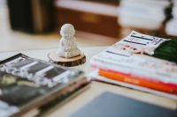 Kaboompics - Small Buddha Figurine on a Wooden Slice Beside Stacked Magazines, Soft-Focus Tabletop Still Life