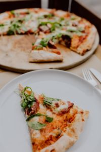 Kaboompics - Pizza Slice on a White Plate with Whole Pizza in Soft Focus