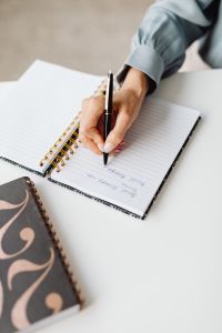 Kaboompics - Close-Up of Asian Woman Writing Notes Beside a Laptop