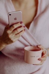A woman in a pink sweater holds a pink iPhone and a pink cup in her hands