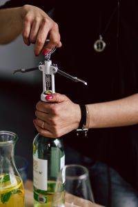 Kaboompics - Close-Up Hands Turning a Corkscrew into a Wine Bottle with Glassware Nearby