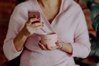 Kaboompics - A woman in a pink sweater holds a pink iPhone and a pink cup in her hands