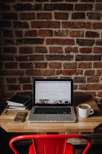 Kaboompics - Creatives desk with laptop, camera, journals and books in front of brick wall
