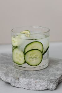 Kaboompics - Minimal Glass of Cucumber and Lime Detox Water on Pale Marble, Centered Summer Drink with Copy Space