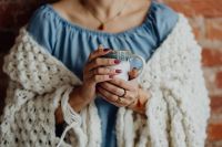Kaboompics - A woman in a warm blanket holds a cup of coffee or tea