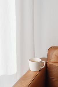 Kaboompics - White Coffee Mug on Tan Leather Sofa with Bright Curtain Copy Space for Cozy Lifestyle Design