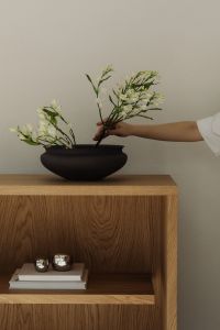 Kaboompics - Hand arranging white flowers in black bowl on oak shelf
